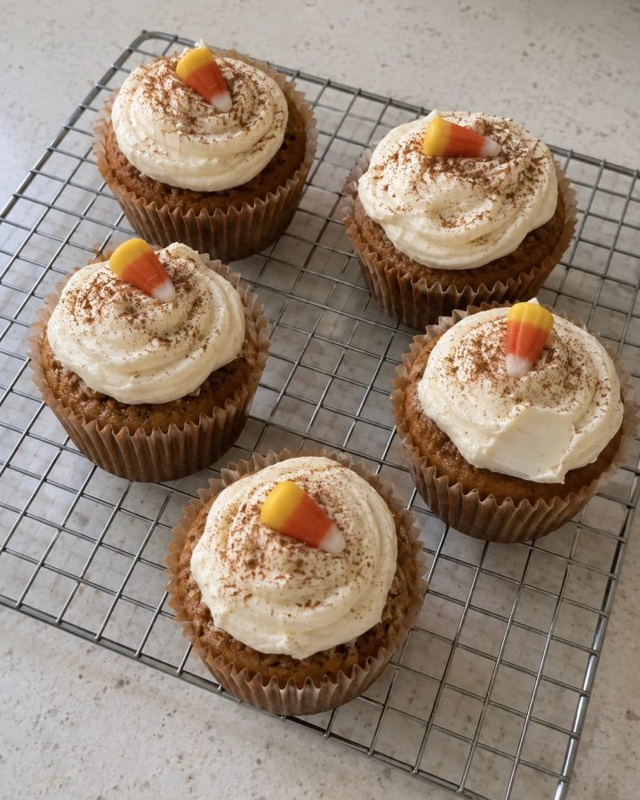 Generated illustration of pumpkin cupcakes on a cooling rack with cream cheese frosting, cinnamon and candy-corn pieces.